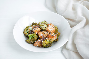 Salad with broccoli and chicken. Hot salad in the sauce served in a white plate. Asian style dish. Light background.