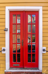 Obraz premium Wooden prehung red front door with white frame, sill, red grilles divide the panes on a house with yellow horizontal siding