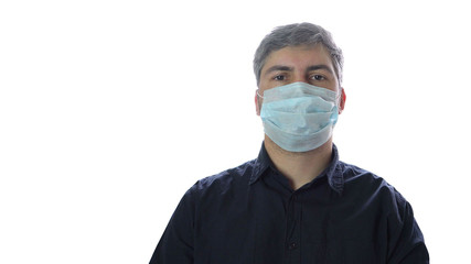 A man in a medical mask stands at the window. Dark shirt. Sick person. Protective equipment. Quarantine. Close-up.