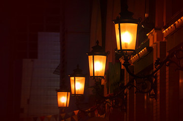 Night street view with glowing real gas lanterns on the outdoor wall. 