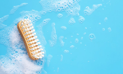 Wooden brush for cleaning clothes with foam of powder detergent water dissolution on blue backgrond.