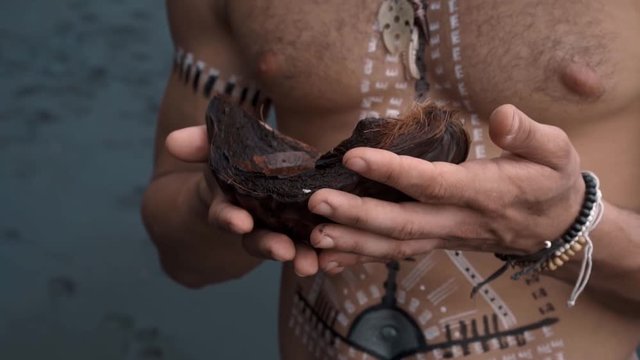 European man with drawings on his body holds a coconut in his hands with water