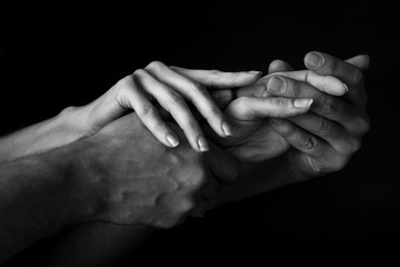 a man holds a woman's hand in his own against a dark background. close up. black and white photo