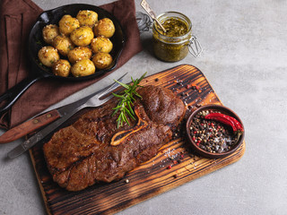 grilled beef steak with bone on a cutting board, roasted new potatoes in a pan