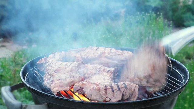 Man cooking meat on black round barbecue grill bbq rotating beaf steaks with open fire smoke