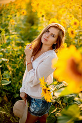 Beautiful woman with long hair walks in a summer sunflower field at sunset