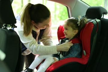 Kid in car seat. Mom and daughter in the car. Mom fastens the child with a safety belt.