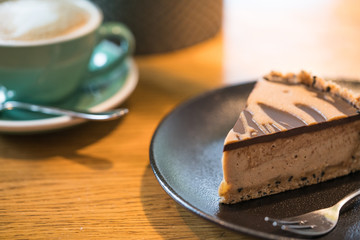 Slice of vegan peanut butter cake in cafe. Green cup with coffee cappuccino