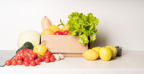 groceries box with vegetables and fruits on white kitchen background. Food delivery services during coronavirus pandemic and social distancing. Shopping online.