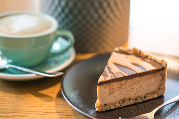 Slice of vegan peanut butter cake in cafe. Green cup with coffee cappuccino