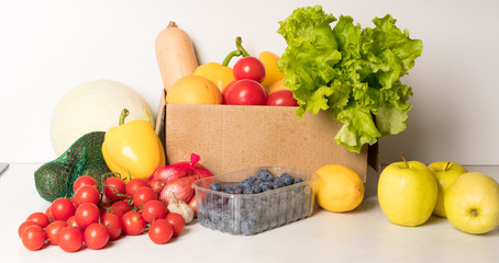groceries box with vegetables and fruits on white kitchen background. Food delivery services during coronavirus pandemic and social distancing. Shopping online.
