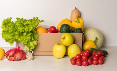 groceries box with vegetables and fruits on white kitchen background. Food delivery services during coronavirus pandemic and social distancing. Shopping online.