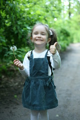 A child in the forest holding a dandelion in his hands.Children alone in the forest.Happy child. Happy little girl. The child goes to school. A child has a backpack on his shoulders.