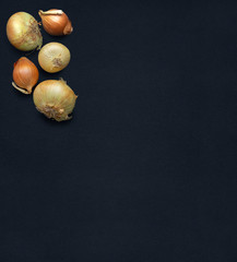 A few onions on a background of natural black textured pastel paper, top view. Space for text, banner, background.