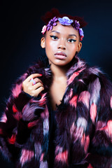 young pretty african american woman in spotted fur coat and flowers jewelry posing on black background