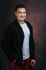 Fototapeta na wymiar Portrait of a young smiling man in a black jacket, white t-shirt, red jeans