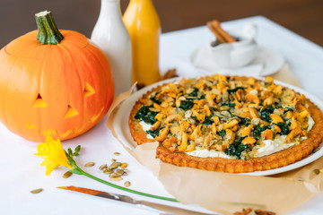 Pumpkin pie with chanterelles. A carved pumpkin in the background. Traditional Halloween dish served on a table with a white tablecloth.