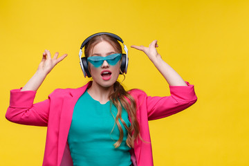 Enjoy listening to music. Young redhead woman in headphones listening music. Funny smiling girl in earphones and pink jacket dancing and singing on yellow background. Relaxation and stress management.