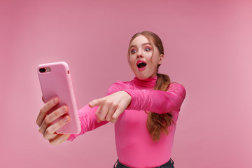 The best day ever. Surpised young redhead woman holding pink smartphone, smiling and expressing positivity. Happy girl got shocking positive news. Copy space. Young people working with mobile devices.
