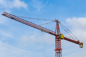 Red tower crane against blue sky with white clouds. Close up. Copy space.
