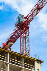 Fototapeta na wymiar One high-rise crane with cab for man against a house and sky during the construction phase. Industry concept for low-income young families. Mortgage, business, real estate loan.