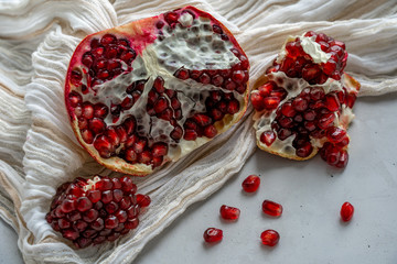 Half of a pomegranate and pomegranate slices and seeds are laying on a beige scarf