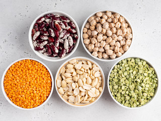 Legumes assortment. Red lentils, dried green peas, chickpeas, red kidney beans in white ceramic bowls on wooden tray. Natural and vegetarian protein food. Copy space. Top view. Concrete background.