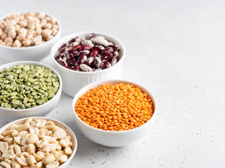 Legumes assortment. Red lentils, dried green peas, chickpeas, red kidney beans in white ceramic bowls on wooden tray. Natural and vegetarian protein food. Copy space. Top view. Concrete background.
