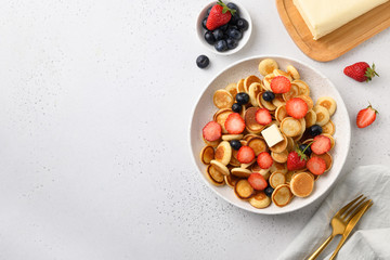 Homemade tiny pancake with blueberry and strawberry on white table. View from above. Copy space. Trendy breakfast.
