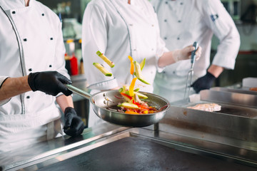 Chefs in protective masks and gloves prepare food in the kitchen of a restaurant or hotel.