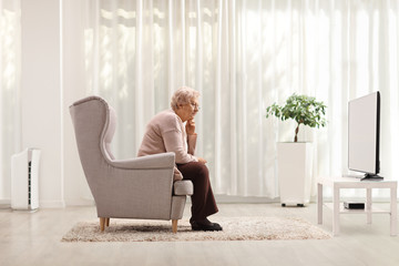 Sad and pensive elderly woman sitting alone in an armchair