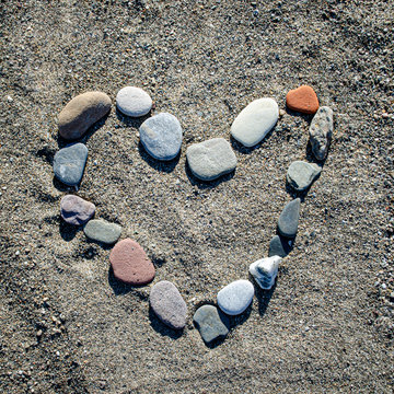 Coloured pebble stones assembled in the form of heart on the sandy beach