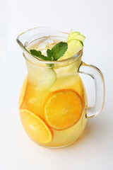 Lemonade of oranges and apples with mint in a tall glass jug on a white background. Top view.