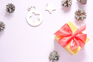 Pine cones near the yellow box with a red bow on a pink background. Flat lay