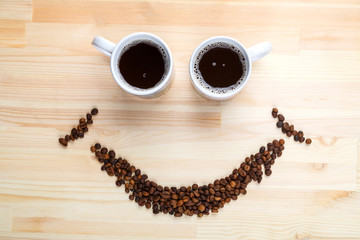 Two cup of coffee on a wooden table and a scattered coffee on the table in the shape of a smile.