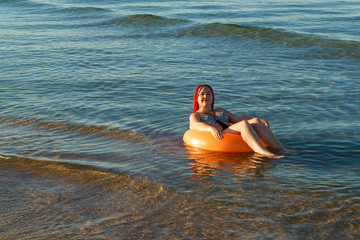 A young woman with African pigtails is sunbathing in an rubber ring in the sea near the shore.