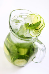 Lemonade made from cucumber slices and green Basil in a tall glass transparent jug on a white background. Vertical photo. An isolated object. Top view.