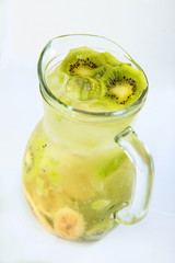 Lemonade of kiwi slices and banana in a tall glass jug on a white background. An isolated object.Top view.