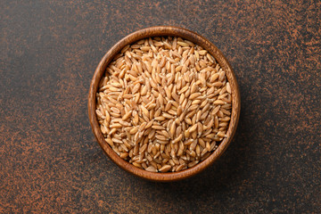 Wholegrain spelt farro in wooden bowl on brown background. Top view.