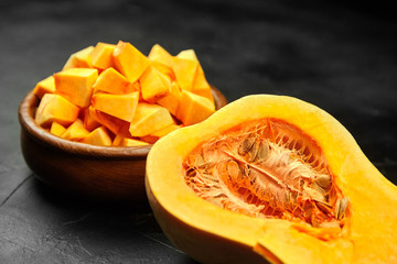 Chopped butternut squash, pumpkin half, fresh vegetable pieces in wooden bowl on black stone table