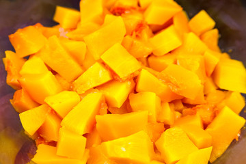 Pumpkin pieces in a deep transparent glass bowl on black table. Chopped pumpkin (butternut squash) in salad dish.