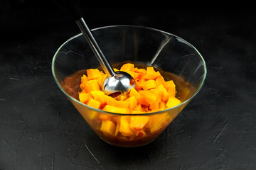 Pumpkin pieces and blender in a glass bowl on black table. Chopped butternut squash, cooking vegetable food, pumpkin puree (mash) recipe