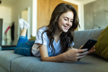 Relaxed girl using a smart phone lying on a sofa in the living room at home