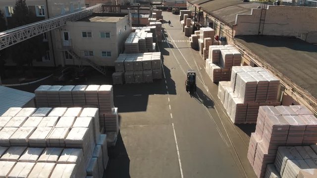 Aerial drone flight over the storage. In the warehouse there are pallets with finished products, cardboard pallets wrapped in plastic film, loaders ride and workers go