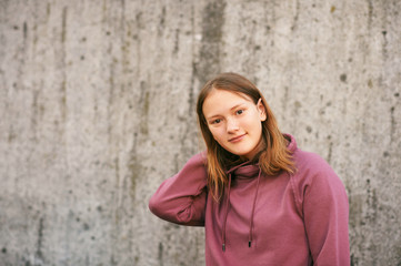 Outdoor urban portrait of young teen girl posing against grey wall, wearing pink sweatshirt