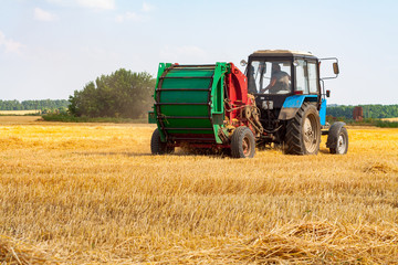 A tractor with a trailed bale making machine collects straw rolls in the field and makes round large bales