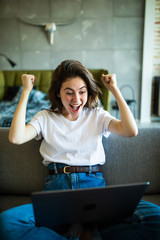 Joyful woman with win gesture using laptop on the sofa