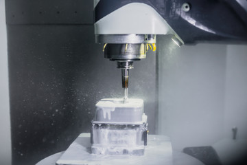 Moderne CNC Fräsmaschine bearbeitet einen Metallblock aus Edelstahl unter Einfluss von Kühlmittel / Emulsion