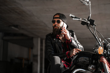 Fototapeta na wymiar Online Internet connection, call, mobile cell phone user. Stylish bearded biker man in black with phone on bike, motorcycle style, brutal man in urban city. Freedom and people lifestyle