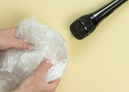 ASMR concept. Specific auditory irritants. Woman's hands wrinkle plastic wrap in front of a microphone. Top view, flat lay.